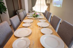 a long wooden table with white plates and chairs at Kokura Family House, 10 Min to Station, 2 Parking, 4 Bed Room in Kitakyushu