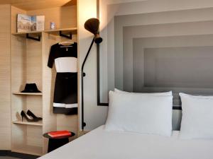 a bedroom with a white bed and a black dress on a shelf at ibis Vichy in Vichy