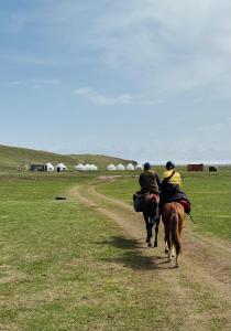 two people riding horses down a dirt road at Ночлег с завтраком in Dzhangyaryk