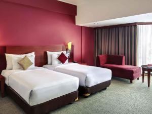 a hotel room with two beds and a chair at Mercure Jakarta Kota in Jakarta
