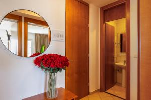 a vase of red flowers on a table in front of a mirror at Hotel Adria in Malinska