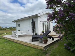 a white house with a wooden deck in the grass at Minihus i lantlig miljö nära havet in Smygehamn