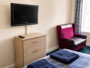 a bedroom with a tv and a chair and a bed at Morlich Guesthouse in Dingwall