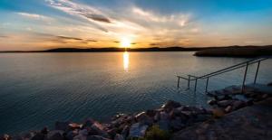 a sunset over a body of water with a dock at Felüdülő Apartman Balatonlelle in Balatonlelle