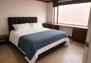 a bedroom with a bed and a desk and a window at Apartamentos Percales in Bogotá