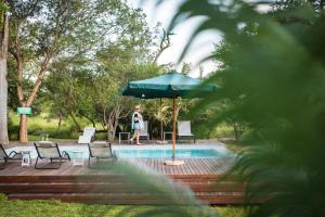 a woman standing next to a pool with an umbrella at Nyala Safari Lodge in Hoedspruit