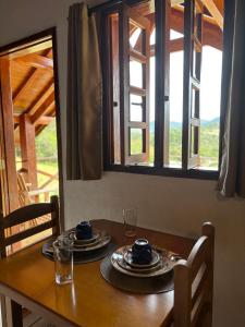 a wooden table with plates and glasses and a window at Chales sol e lua in Camanducaia