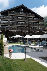 a large hotel with a pool and chairs and umbrellas at Mirabeau Alpine in Zermatt
