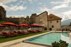 a resort pool with red chairs and umbrellas at Castel Badia - The Leading Hotels of the World in San Lorenzo di Sebato