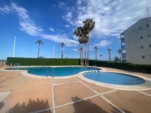 a swimming pool with palm trees and a building at Terra marina in Grao de Castellón