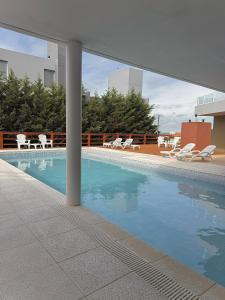 a swimming pool with white chairs and a building at Zelena Voda in Villa Gesell