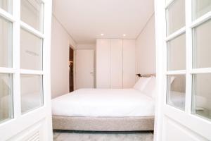 a white bedroom with a bed and large windows at Micah's Biscainhos Apartment by Quantique in Braga