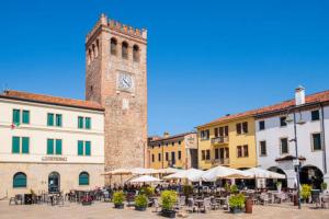 a clock tower in a town with tables and umbrellas at Casa Mazzini in Monselice