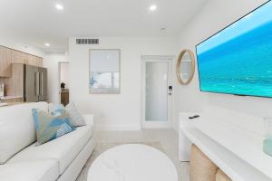 a white living room with a white couch and a large tv at Casa Coral - Boca Poolside Escape in Boca Raton