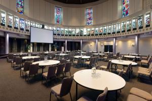 a large room with tables and chairs and stained glass windows at NH Noordwijk Conference Centre Leeuwenhorst in Noordwijkerhout