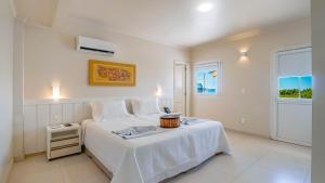 a white bedroom with a bed and a window at Hotel Vila do Farol in Bombinhas