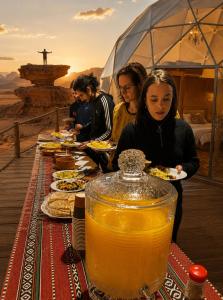 a group of people eating food at a table with drinks at Wadi Rum Faris in Wadi Rum