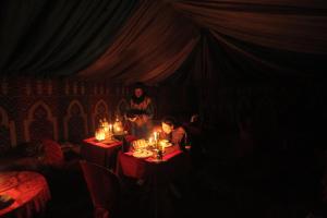 een groep mensen die aan tafel zitten in een kamer met kaarsen bij Bivouac Karim Sahara in Zagora