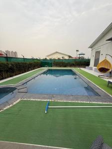 a swimming pool with a green lawn and a building at oliv Faram house in Greater Noida +17 photos