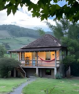 a house with a porch and a staircase in a field at Piccola Cucina: Casa centenária Vale dos Vinhedos in Garibaldi