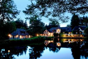 une maison éclairée sur l'eau la nuit dans l'établissement Au Moulin de La Gorce, à La Roche-lʼAbeille