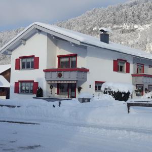 Un bâtiment blanc avec des fenêtres rouges dans la neige dans l'établissement Appartements Gästehaus Monika, à Bezau