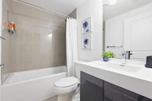 a white bathroom with a toilet and a tub and a sink at Charming 2BR downtown condo with private patio in Toronto