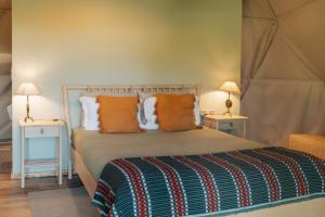 a bedroom with a bed with orange pillows and two tables at Manteiros Glamping in Canas de Senhorim