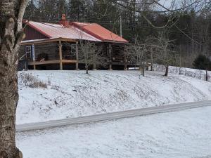 a log cabin in the snow with a road in front at Mountain Memories Cabin Rental in Booneville