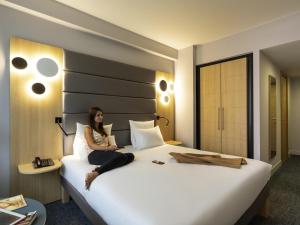 a woman sitting on a bed in a hotel room at Novotel Brussels Centre Midi in Brussels +49 photos