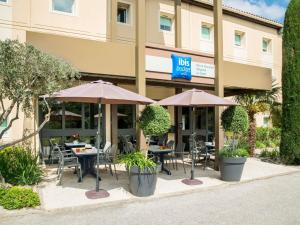 a hotel with tables and chairs and umbrellas at IBIS Budget Aix en Provence Est Le Canet in Meyreuil