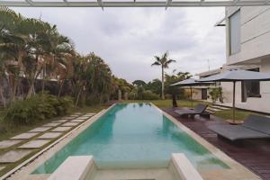 an infinity pool with chairs and an umbrella next to a house at Nara Villa Canggu by Ini Vie Hospitality in Canggu