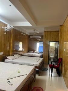 a bedroom with two beds and a red chair at Panthanibas momochitte in Bakkhali