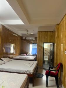 a bedroom with two beds and a red chair at Panthanibas momochitte in Bakkhali