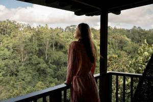 a woman standing on a balcony looking out at the forest at Nandini Jungle by Hanging Gardens in Payangan