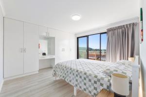 a white bedroom with a bed and a large window at Forsters Bay Haven in Narooma