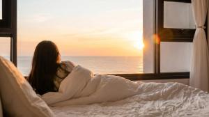 a woman laying in bed looking out a window at the ocean at Pohang Pine Wave Pension in Pohang