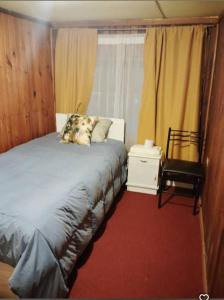a bedroom with a bed and a chair and a window at Pensión San Andrés in Concepción