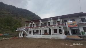 a large white building with a mountain in the background at Swastik Hotel & Restaurant in Kharsālī