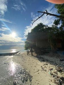a shack on a beach with the sun in the sky at Kainora Homestay in Dayang