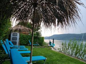 a group of blue lounge chairs under a straw umbrella at Ferienhaus AUEN mit Seezugang in Velden am Wörthersee
