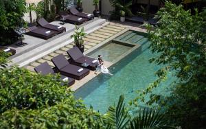 a woman standing next to a swimming pool with lounge chairs at Indochine Serenity Boutique in Siem Reap