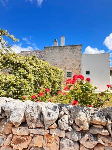 a stone wall in front of a building with red flowers at Giardino dei Trulli Cummerse in Faccia di Trippa di Monte