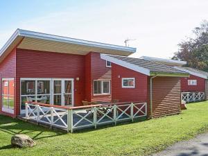 a red cabin with a porch and a yard at Danland Rø Golf Houses in Gudhjem