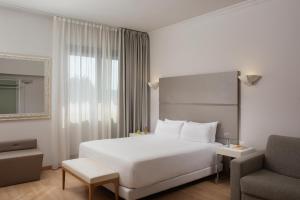a white bedroom with a large bed and a chair at NH Ancona in Ancona