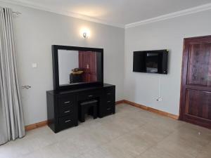 a room with a dresser with a mirror and a television at Ivory & Mane Estate - Jacaranda in Harare