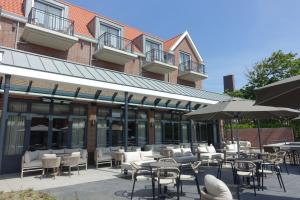a patio with chairs and tables and umbrellas in front of a building at Hotel The Dunes in Domburg