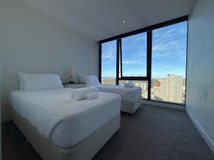 a white bedroom with two beds and a large window at Southbank Sanctum in Melbourne