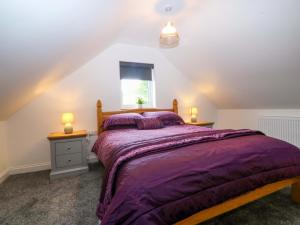a bedroom with a bed with purple comforter and a window at Ty Loti in Caernarfon