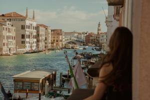 a woman looking out a window at a canal with boats at Sina Palazzo Sant'Angelo in Venice